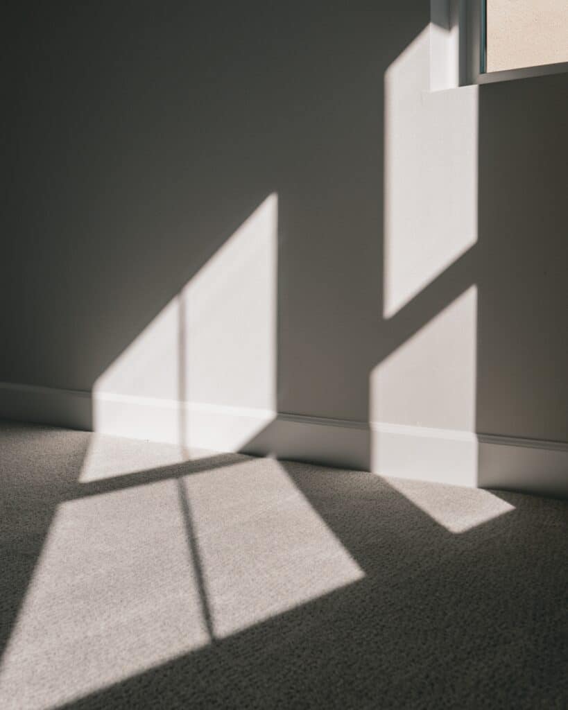 A view of grey carpet in a shadow filled room.